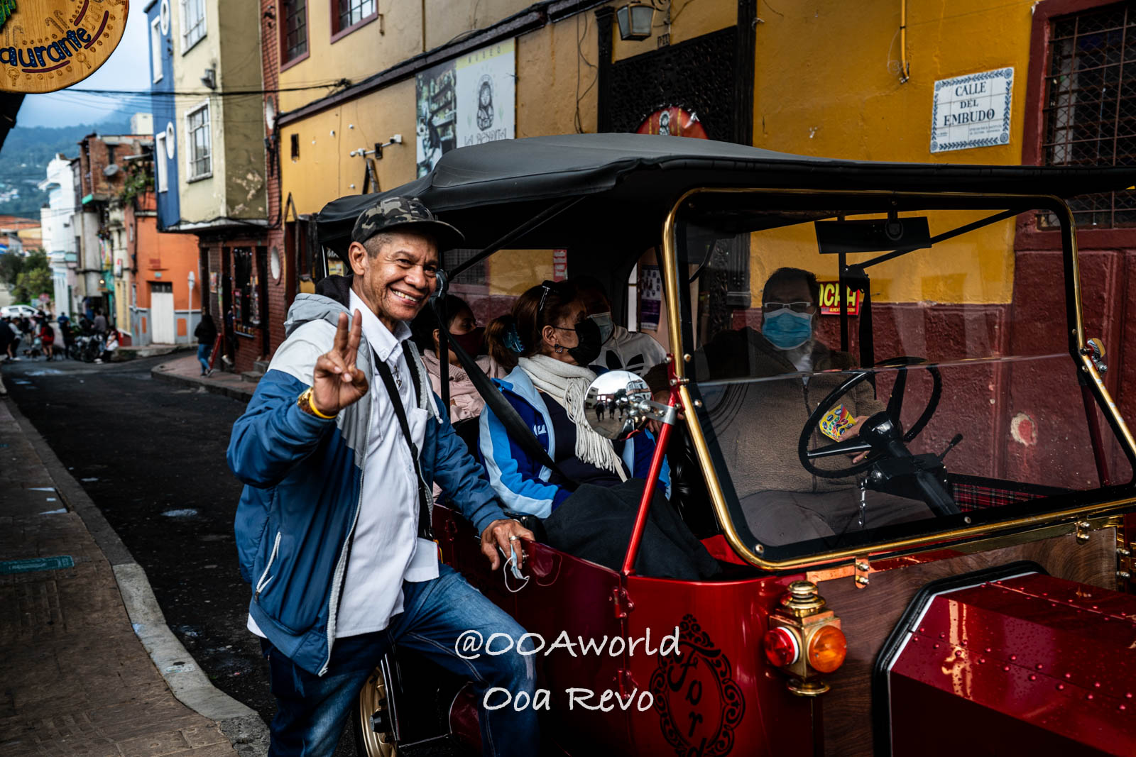 La Candelaria Bogota smiling man with peace sign beside red vehicle on colorful street Photo OOAworld