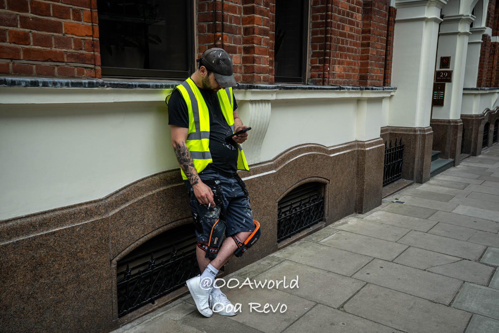 London People and Streets London construction worker leaning on building wall in yellow safety vest urban setting Photo OOAworld