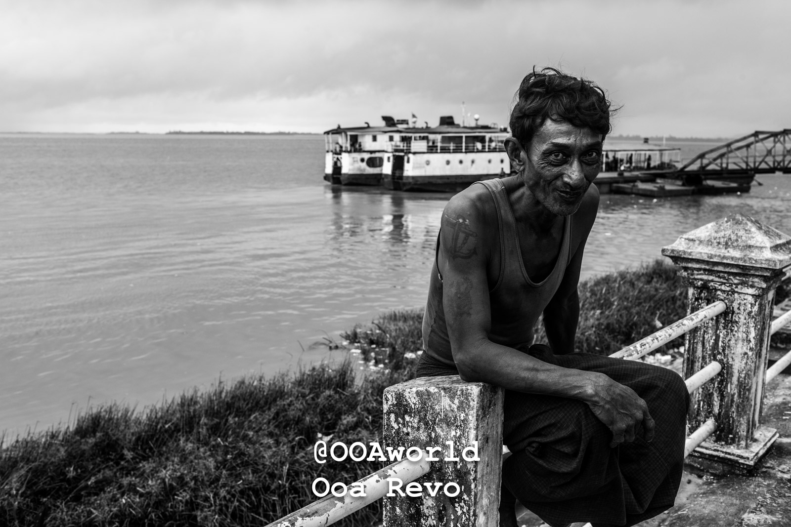 Mawlamyine Myanmar Man sitting by a river with boat in background black and white Photo OOAworld