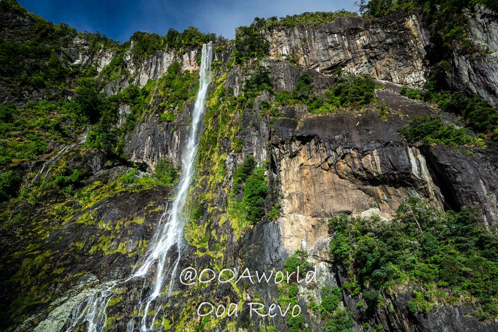 Milford Sound Fjord New Zealand stunning waterfall cascading down rocky cliff surrounded by lush greenery Photo OOAworld