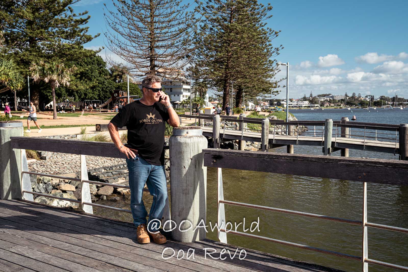 Byron Bay, Port Macquarie Australia man standing on boardwalk by waterfront park with trees and blue sky Photo OOAworld