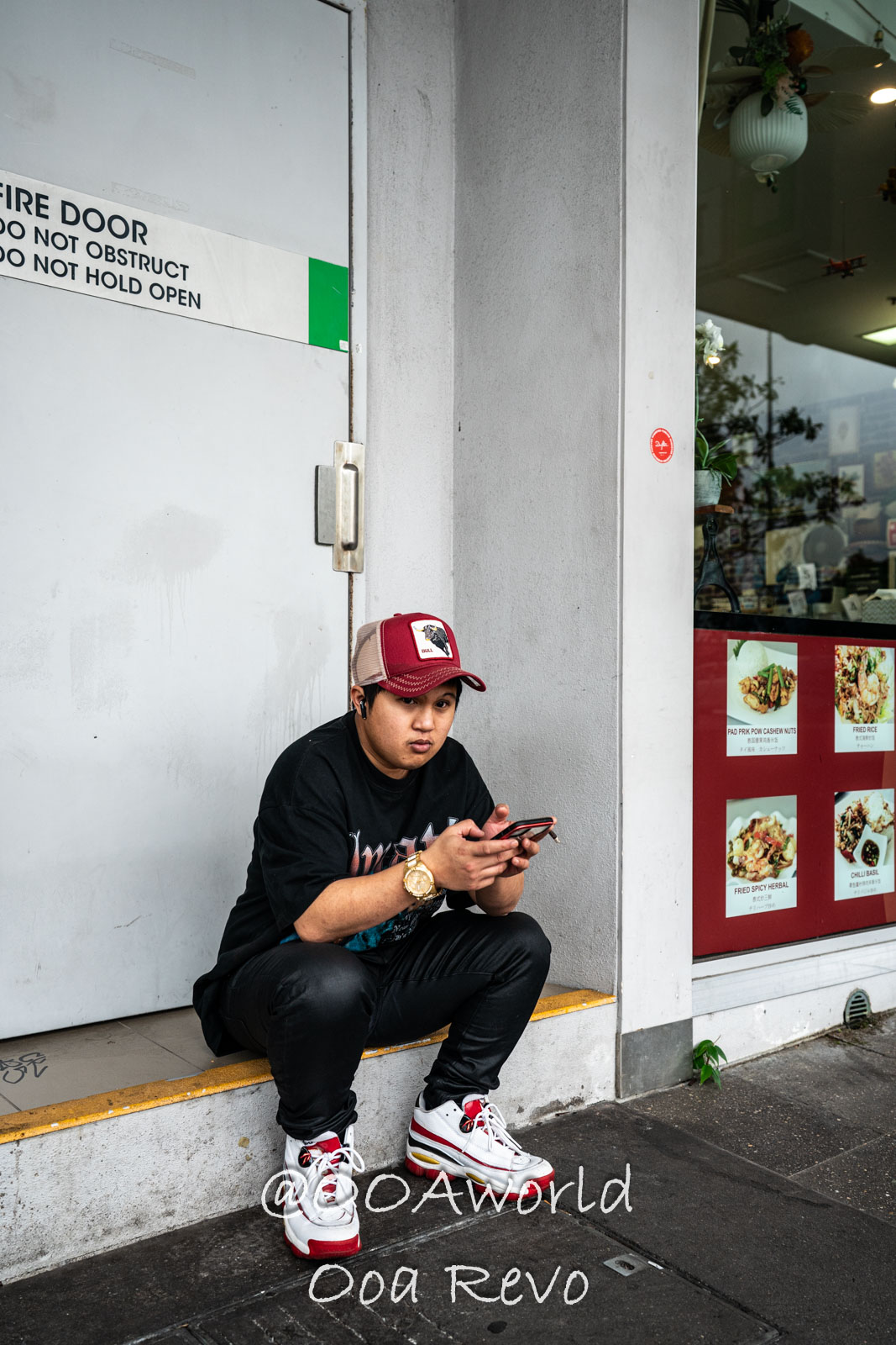 Cairns Australia man sitting outside restaurant with phone and cap Photo OOAworld