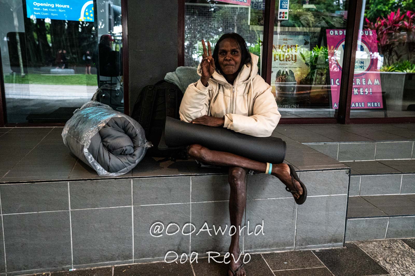 Cairns Australia elderly person sitting outside shop with peace sign Photo OOAworld