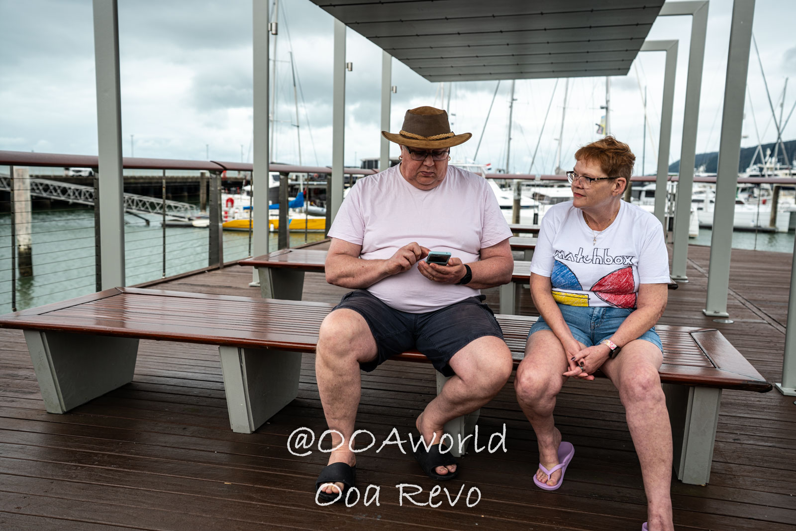 Cairns Australia couple sitting on marina bench looking at phone Photo OOAworld